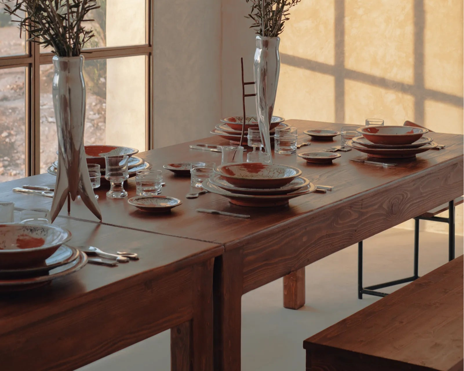Dining room with a long wooden table set for a meal, large windows allowing natural light to fill the space.